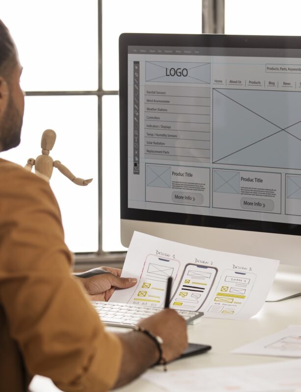 UX Designer Developer comparing printed UX design to mockup on computer screen.