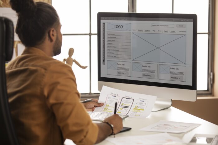 Developer comparing printed UX design to mockup on computer screen.