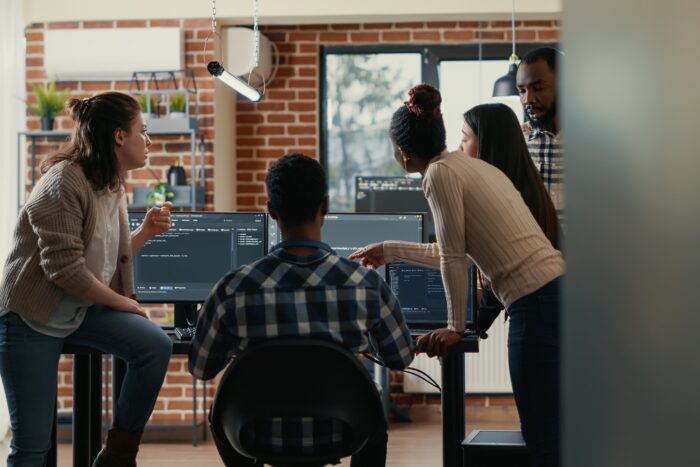 Development team standing around computer monitors in a discussion.