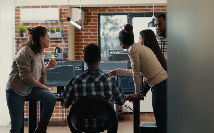 Development team standing around computer monitors in a discussion.