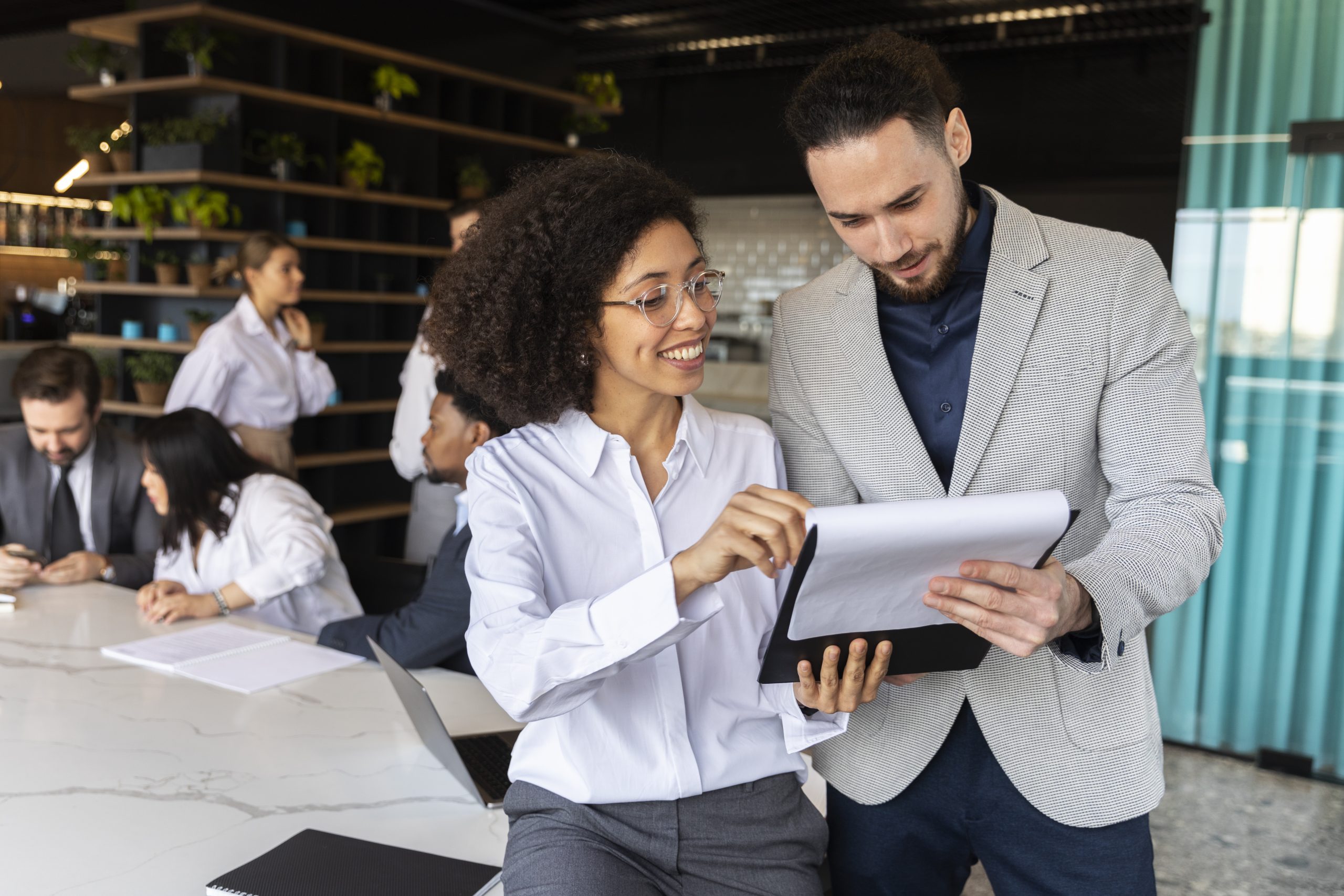 A woman and man holding a notepad in front of a conference table.