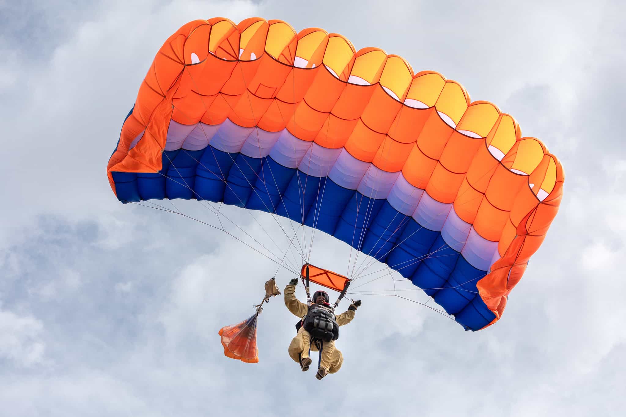 Great Basin Smokejumpers Training. Smokejumper parachuting with cloudy sky behind him.