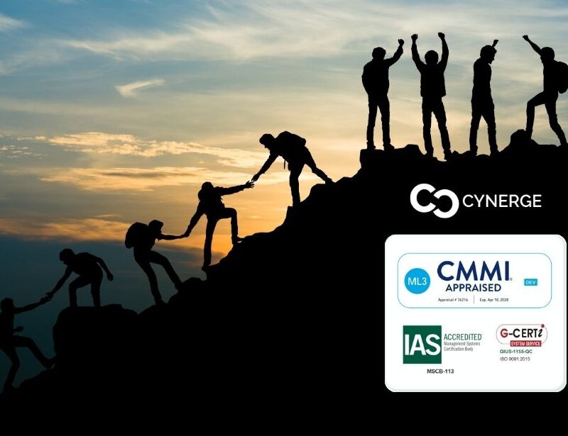 Silhouette of a team climbing a mountain, celebrating success getting to the top. The background shows the sky at dawn. The Cynerge logo appears above CMMI and ISO 9001:2015 badges.