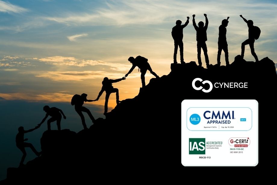 Silhouette of a team climbing a mountain, celebrating success getting to the top. The background shows the sky at dawn. The Cynerge logo appears above CMMI and ISO 9001:2015 badges.